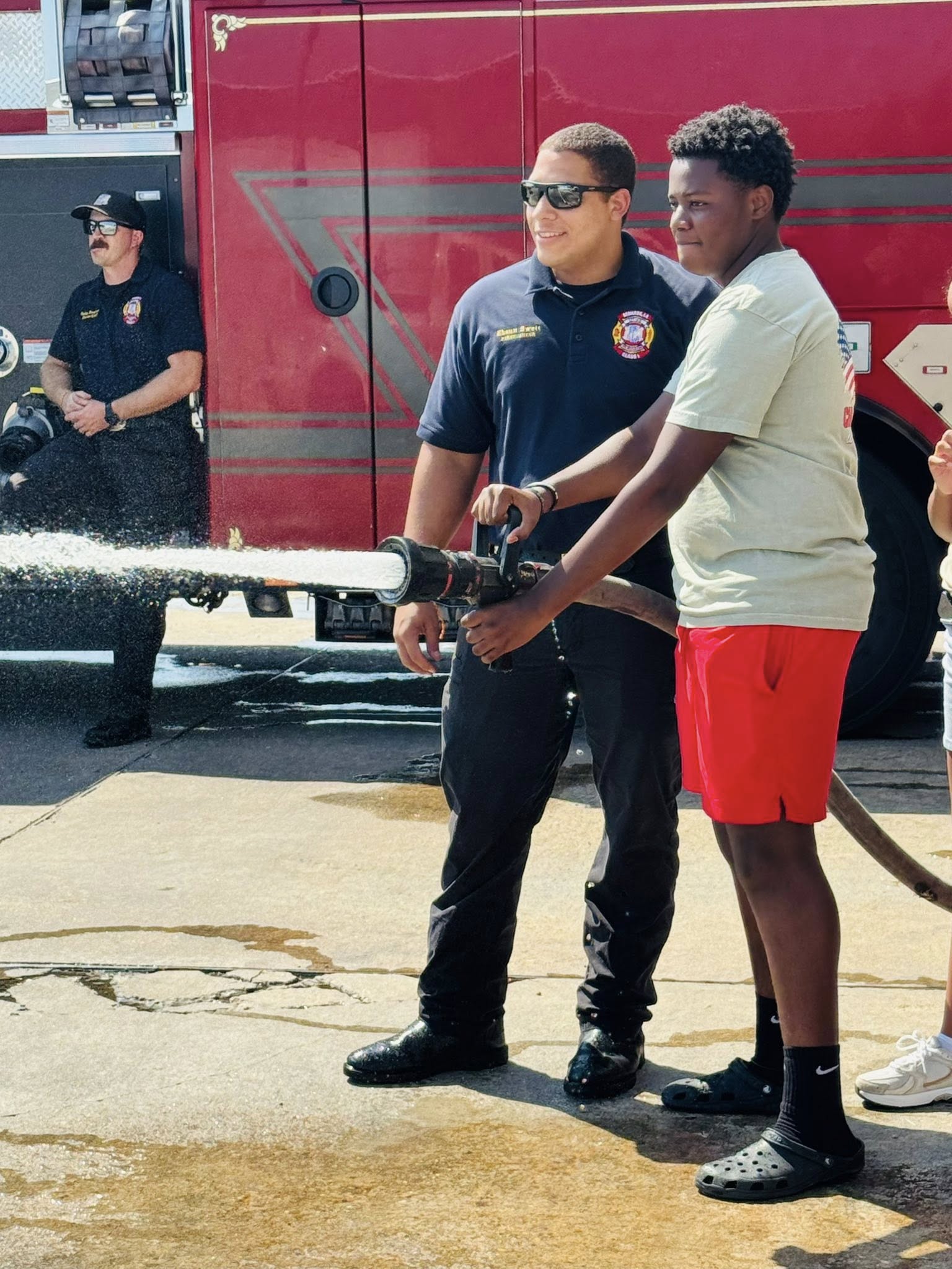 A fireman letting a boy work a firehose.